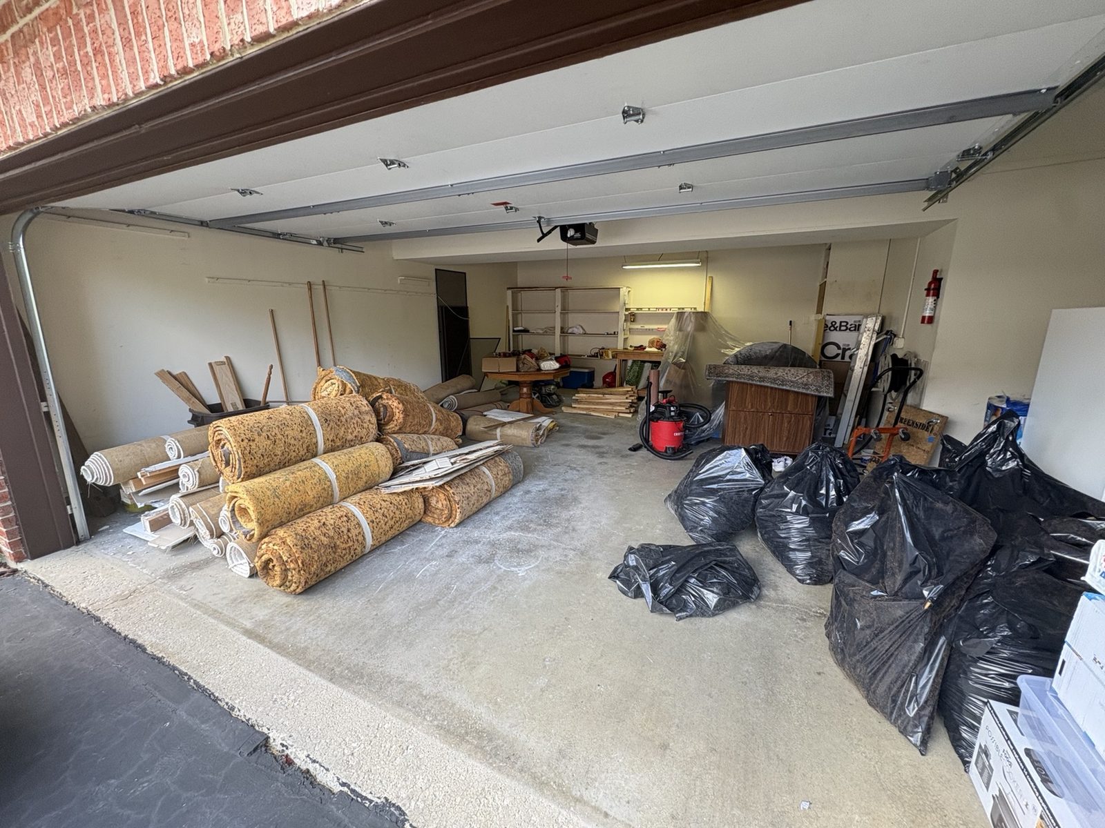 Garage full of carpet rolls, trash bags and leftover materials before cleaning